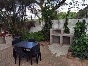 Un patio al aire libre con una mesa y sillas de ladrillo, una parrilla y un horno de piedra.