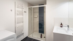 Un baño moderno con ducha envuelta en vidrio, un lavamanos blanco y un calentador integrado.