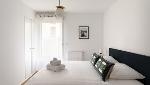 Un dormitorio con una cama, un radiador, un cuadro enmarcado en la pared y una ventana con cortinas.