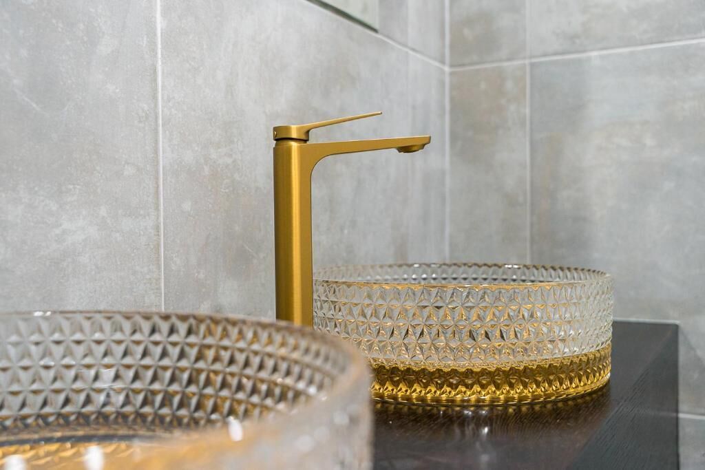 Une salle de bain avec un robinet doré et deux bols en verre texturé posés sur un plan de toilette foncé.