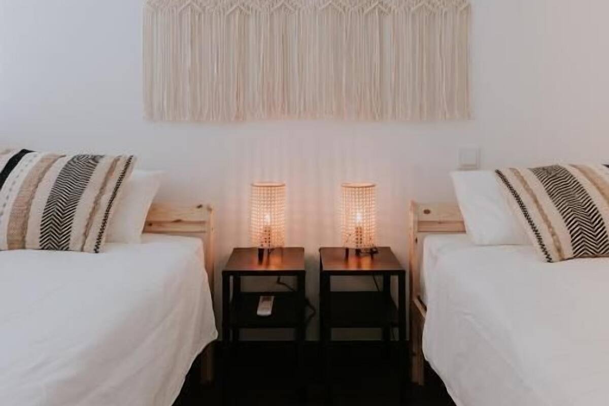 A bedroom with two beds, a macrame wall hanging, and bedside lamps.
