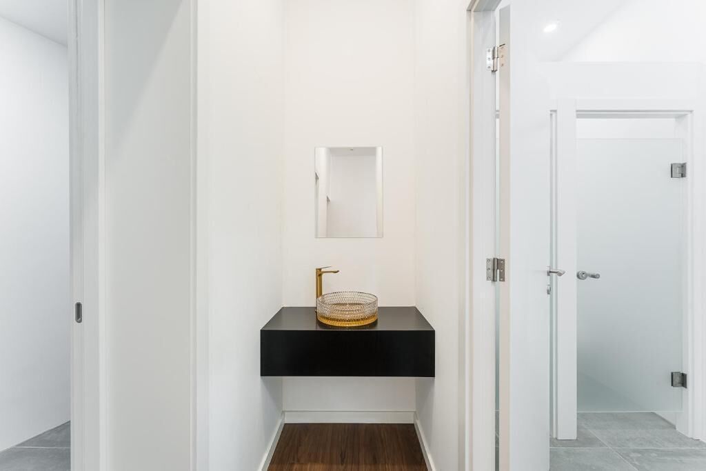 Een moderne badkamer met een zwart aanrechtblad, een gouden kraan en een spiegel boven de wastafel.