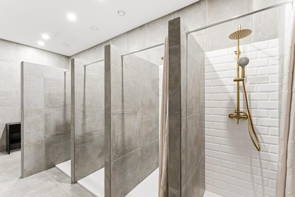 A modern bathroom with a glass-enclosed shower area, a gold showerhead, and a tiled wall.