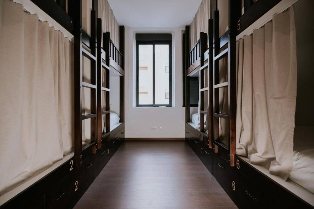 A dormitory room with bunk beds, a window, and a door.