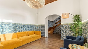Un'ampia hall con un divano giallo, pareti a motivi blu, una scala e un soffitto in legno.