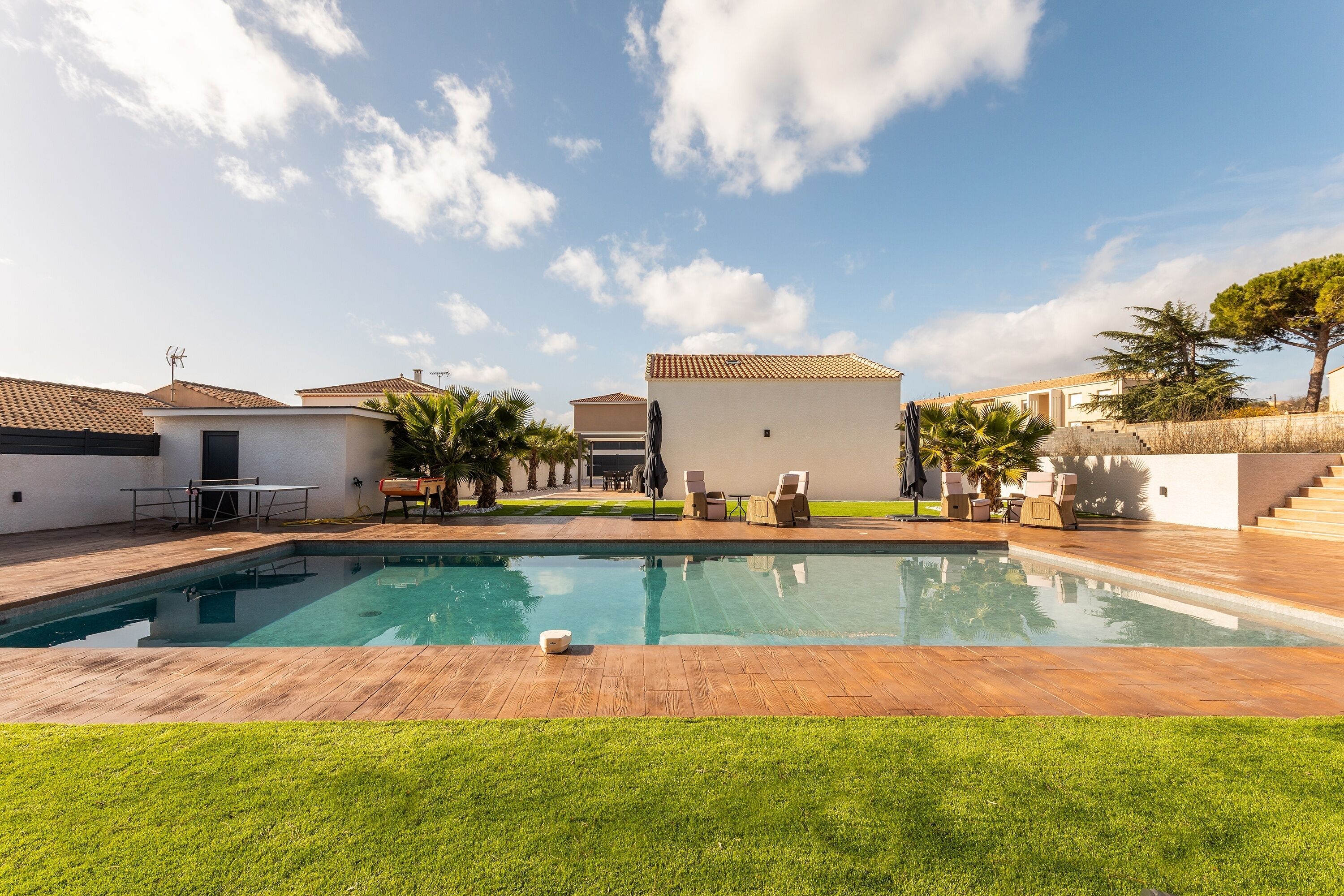 A swimming pool with a wooden deck, surrounded by a well-maintained lawn and palm trees.