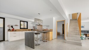 Una cocina moderna con una isla central, taburetes de bar y una escalera que sube a otro nivel.