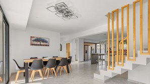 Una cocina moderna con una isla central, un comedor con mesa y sillas de madera, y una escalera con detalles de madera.