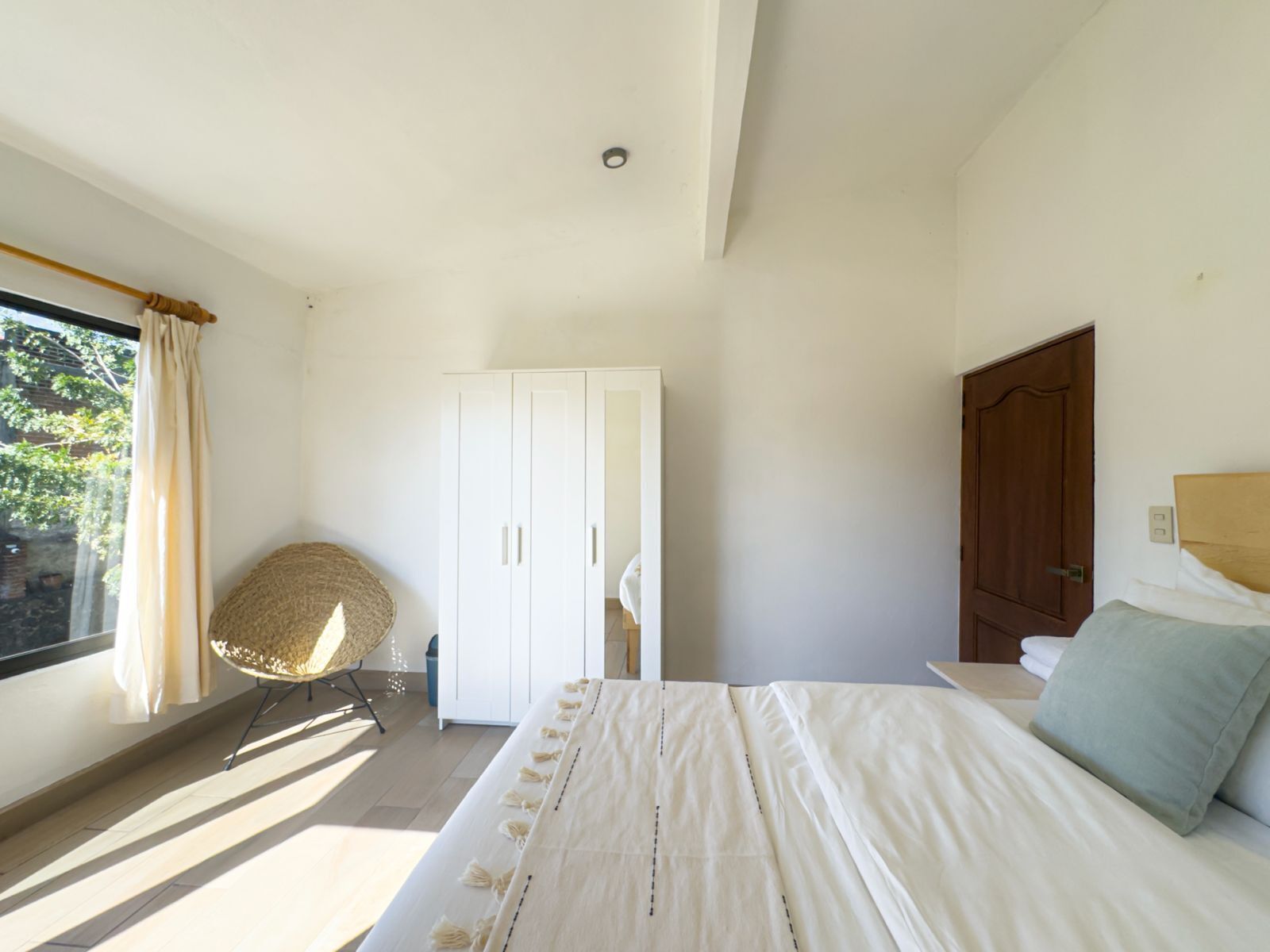 A bedroom with a bed, a wardrobe, a window with curtains, and a chair.