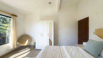 A bedroom with a bed, a wardrobe, a window with curtains, and a chair.