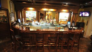 A bar area with a long counter, multiple stools, and a television mounted on the wall. - Spacious 3 King Suite with Pools, Grill & Bar Near Laredo Dining & Shops (Laredo)
