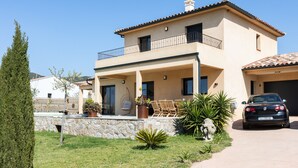 A two-story house with a balcony, a car parked in front, and a stone wall.