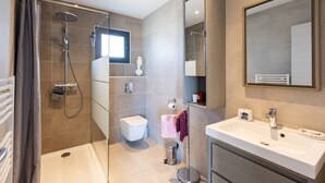 A modern bathroom with a shower, toilet, sink, and a large mirror.