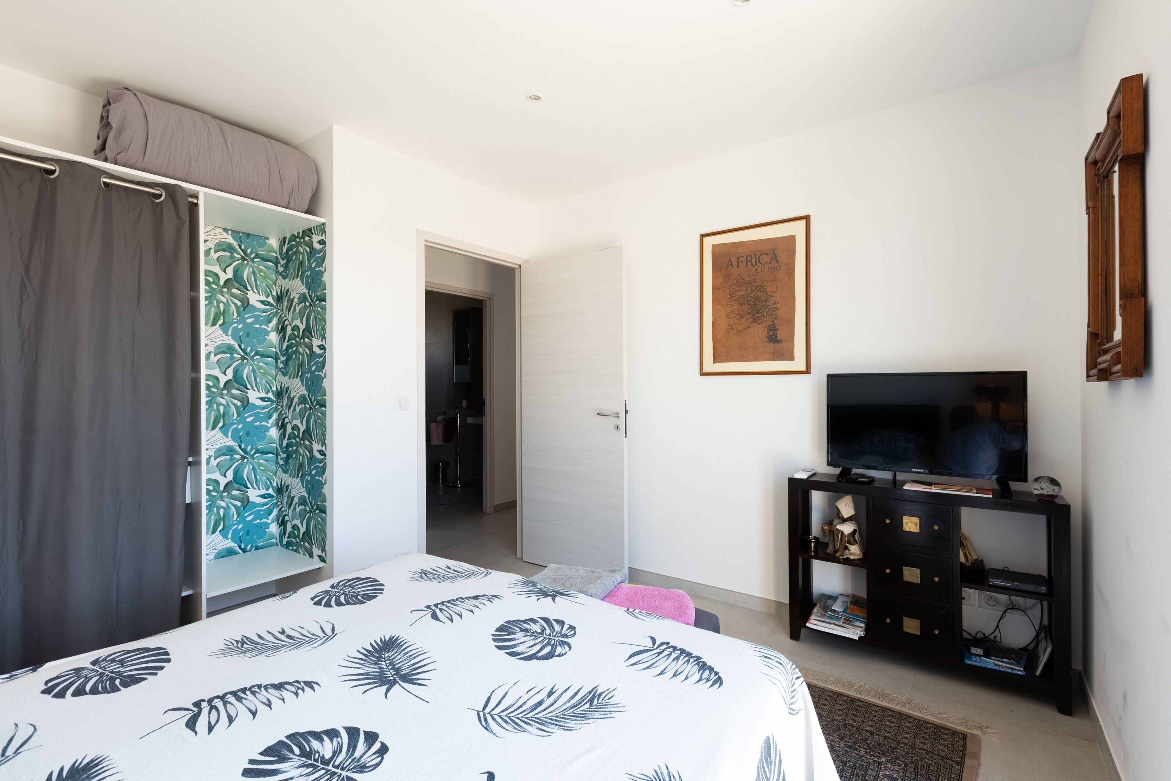 Een slaapkamer met een bed, een kledingkast, een televisie en een lijst aan de muur.