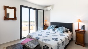 A bedroom with a bed, two bedside lamps, a nightstand, a mirror, and a sliding glass door leading to a balcony.