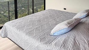 Une chambre avec un grand lit, une vue sur les montagnes par la fenêtre et un luminaire suspendu.