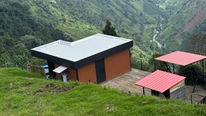 Un bâtiment moderne doté d’un toit plat, entouré de collines verdoyantes et bordé par une rivière.