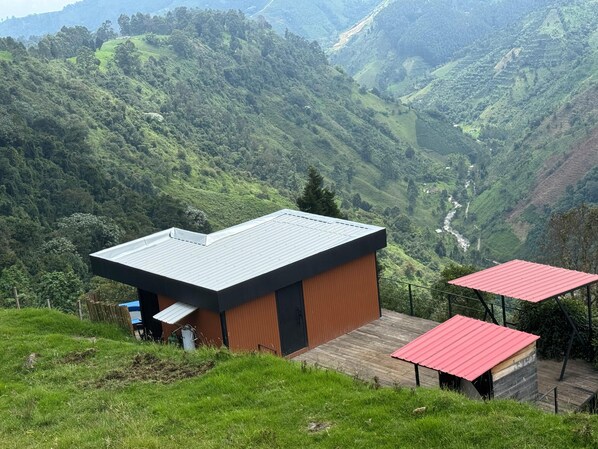 A modern building with a flat roof, surrounded by lush green hills and a river. - Glamping Canoas Santa Rosa de Cabal (Santa Rosa de Cabal)