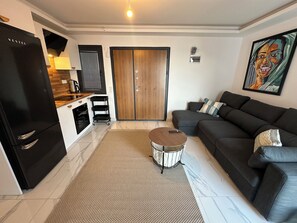 A modern living room with a black refrigerator, a grey sofa, and a coffee table.