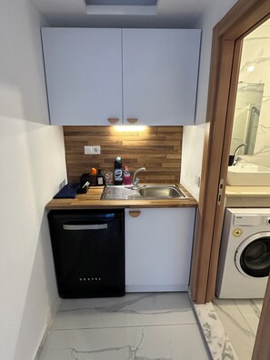 A compact kitchen with white cabinets, a wooden countertop, a dishwasher, and a washing machine.