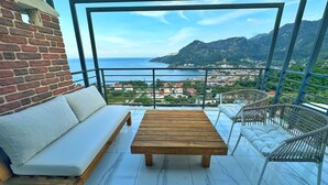 A balcony with a wooden table and a sofa, overlooking a coastal town and mountains. - SWEET HOME TURUNC - The Penthouse (Muğla)
