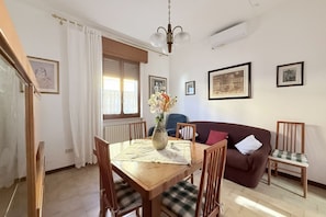 Un coin repas avec une table en bois, des chaises, un vase de fleurs, un canapé et des tableaux encadrés au mur.