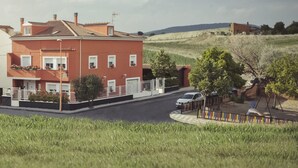 A red two-story house with a tiled roof, a white car parked in front, and a grassy hill in the background. - RURAL HOUSE THE WILLOW. 2.5 km from the city of Cuenca. Groups of up to 23 people (Nohales)