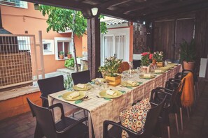 Un espace de restauration en plein air avec une longue table dressée pour un repas, entourée de chaises et agrémentée de plantes en pot.