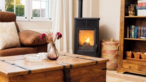A cozy living room with a wooden chest, a vase with flowers, a bookshelf, and a wood-burning stove. - RURAL HOUSE THE WILLOW. 2.5 km from the city of Cuenca. Groups of up to 23 people (Nohales)