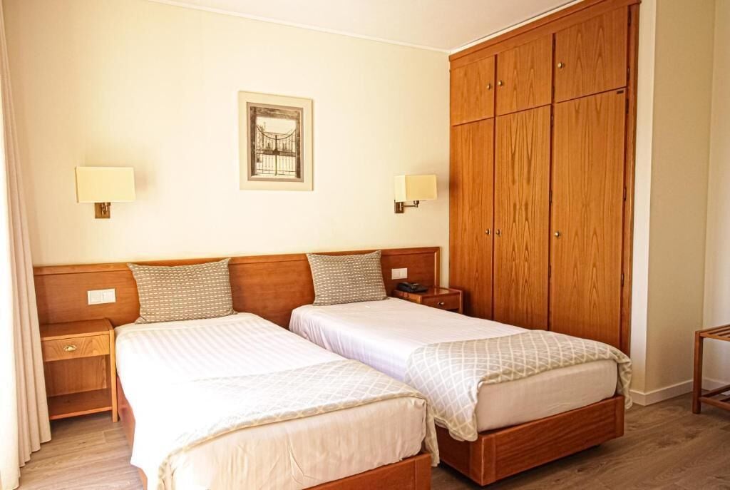 A hotel room with two beds, wooden wardrobe, bedside lamps, and a framed picture on the wall.