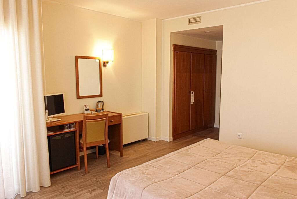 Habitación de hotel con cama, escritorio con silla, televisor y armario de madera.