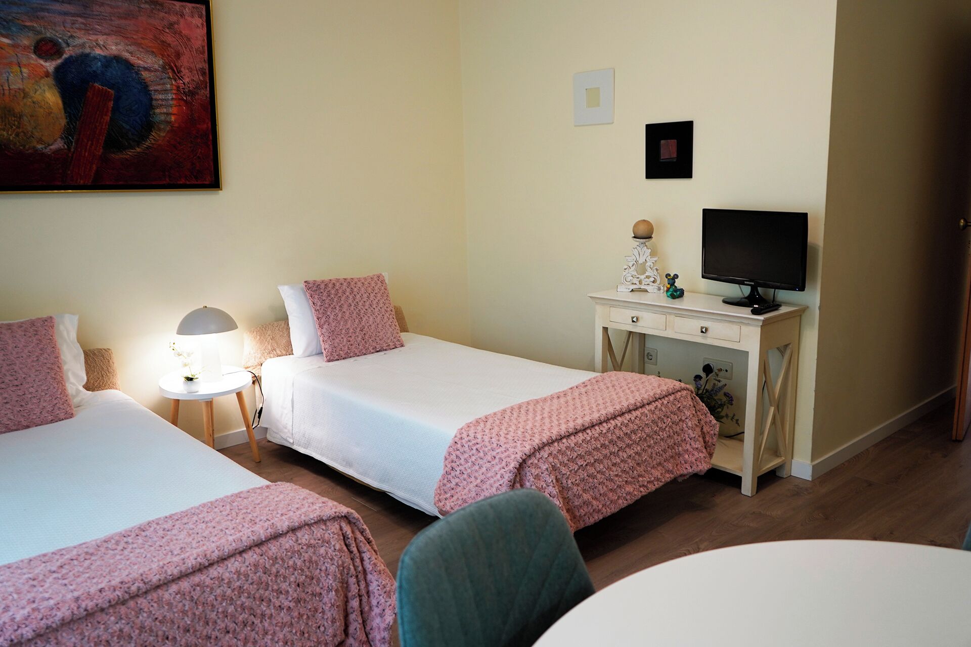 Habitación de hotel con dos camas, un escritorio con computadora, una lámpara y un cuadro en la pared.