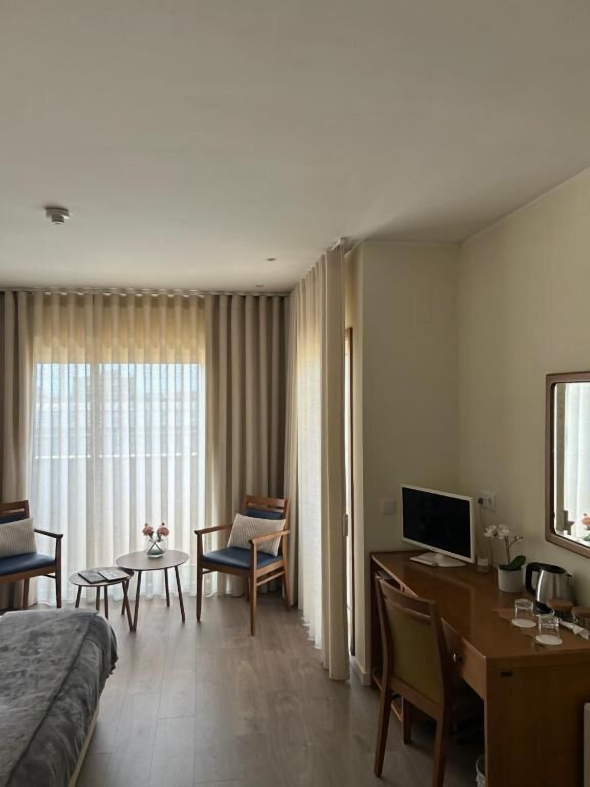 Une chambre d’hôtel comprenant un lit, un bureau, deux chaises, une petite table avec un vase et un téléviseur.