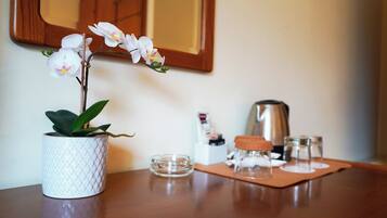 Un jarrón blanco texturizado con una orquídea sobre una mesa de madera, un pequeño cuenco de vidrio, un hervidor metálico y un vaso con tapón de corcho sobre un tapete de corcho.