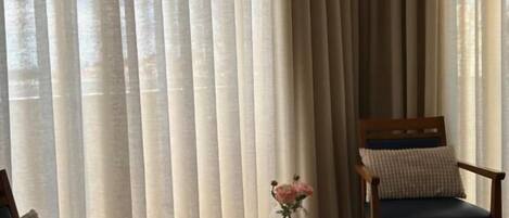 Una habitación con dos sillas de madera, una mesita redonda con un florero y cortinas translúcidas.