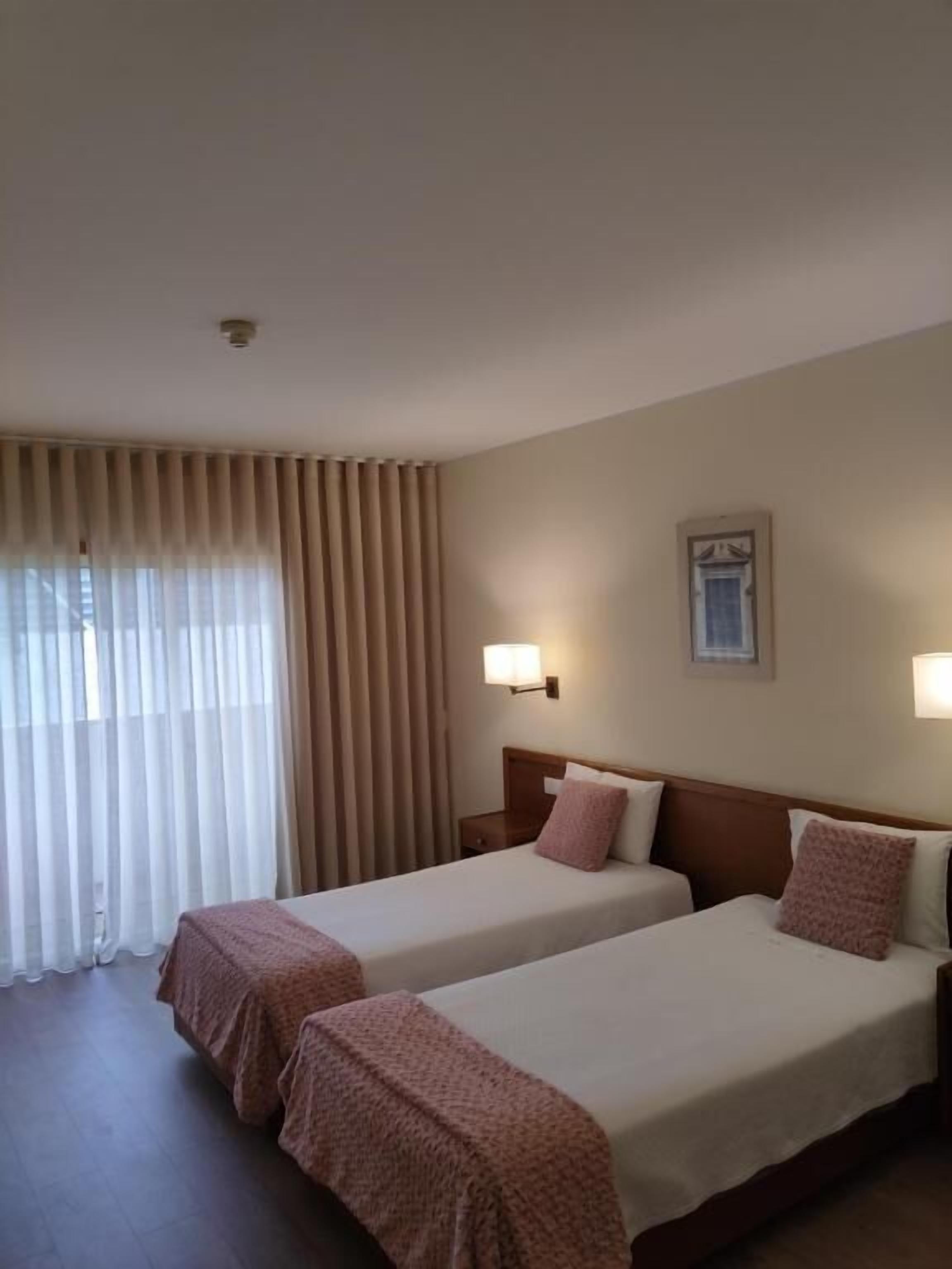 Habitación de hotel con dos camas, paredes color beige y una ventana con cortinas.