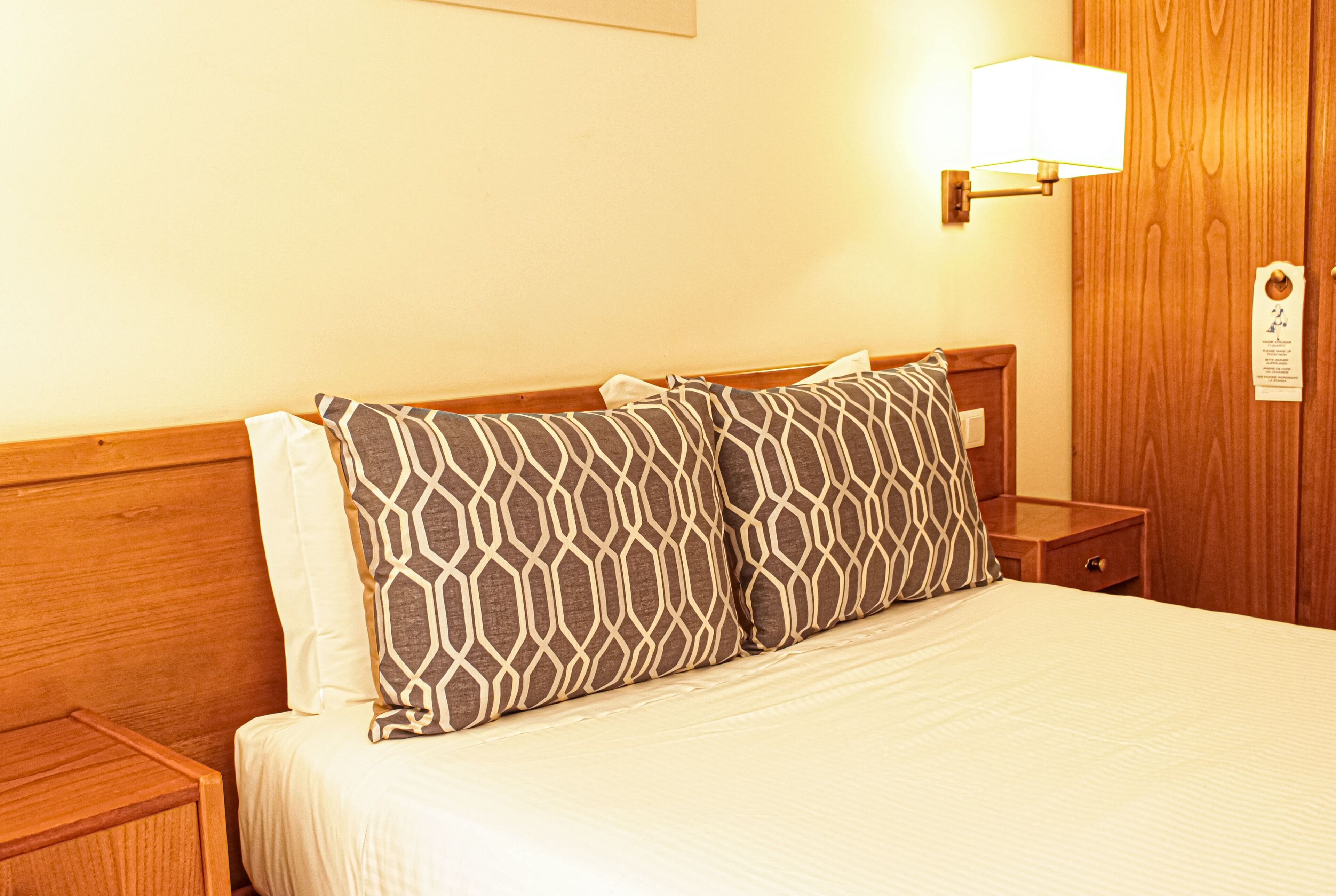 A neatly made bed with patterned pillows, a bedside lamp, and a wooden nightstand.