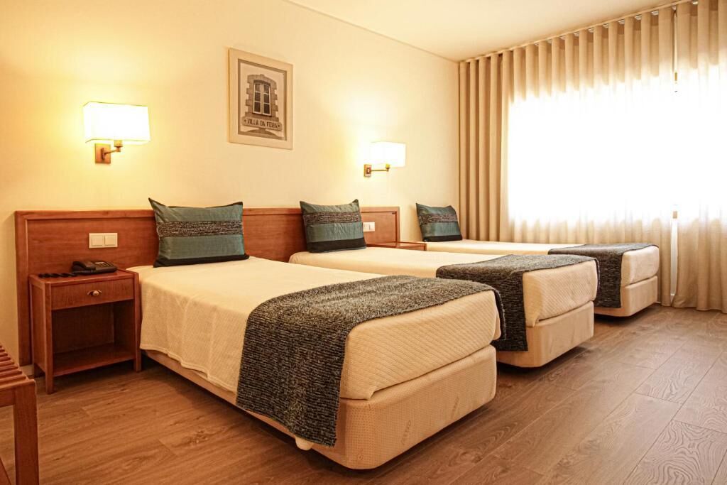 A hotel room with two beds, each with a headboard, bedside tables, and lamps.