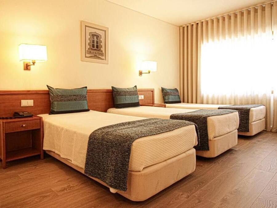 A hotel room with two beds, each with a headboard, bedside tables, and lamps.