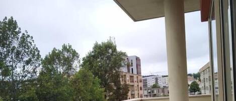 A balcony with two black chairs and a small table, overlooking a cityscape with buildings and trees.