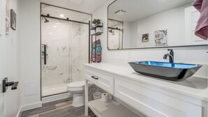Een moderne badkamer met een douchecabine van glas, een witte wastafel met een blauwe wasbak en een grote spiegel boven het aanrecht.