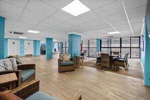 Un espacio interior amplio con mobiliario de mimbre, una mesa de comedor y ventanas grandes.