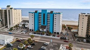 Ett hotell med flera våningar, med en framträdande blå och vit fasad, som ligger nära en strand och har en parkeringsplats på förhand.