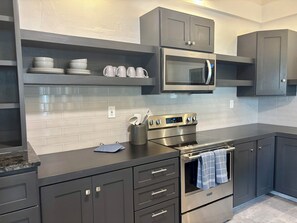 A modern kitchen with grey cabinetry, a stainless steel stove, a microwave, and a tiled backsplash. - Sib's Crystal Charm  - The Coziest In Town. (Charlotte Amalie)