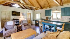 A cozy cabin interior with a wooden ceiling, a fireplace, a dining area, and a kitchen with blue cabinets. - Pet-Friendly Cottage w/ Hot Tub Lake Koocanusa (Rexford)