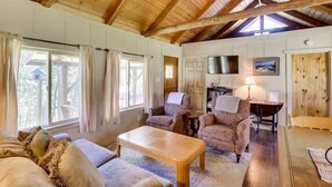 A cozy living room with wooden beams, a sofa, armchairs, a coffee table, and a TV. - Pet-Friendly Cottage w/ Hot Tub Lake Koocanusa (Rexford)