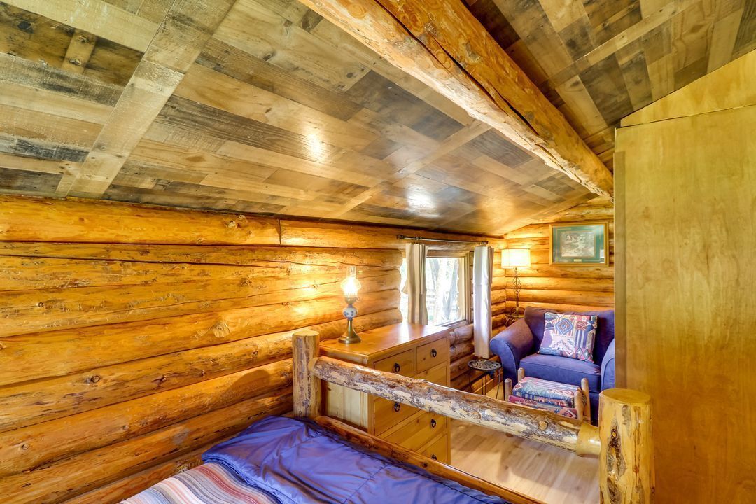 L’intérieur d’une cabane en rondins, avec un lit, une petite table, une chaise et une fenêtre.