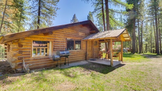 Una cabaña de troncos con porche y zona de barbacoa, rodeada de un bosque.