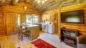 Interior de una cabaña de troncos con cocina, comedor y televisor de pantalla plana.