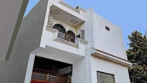 A building with a white facade, a balcony with decorative railings, and a window with a decorative grille. - Hotel O Sant Ravidas Ghat Varanasi (Varanasi)